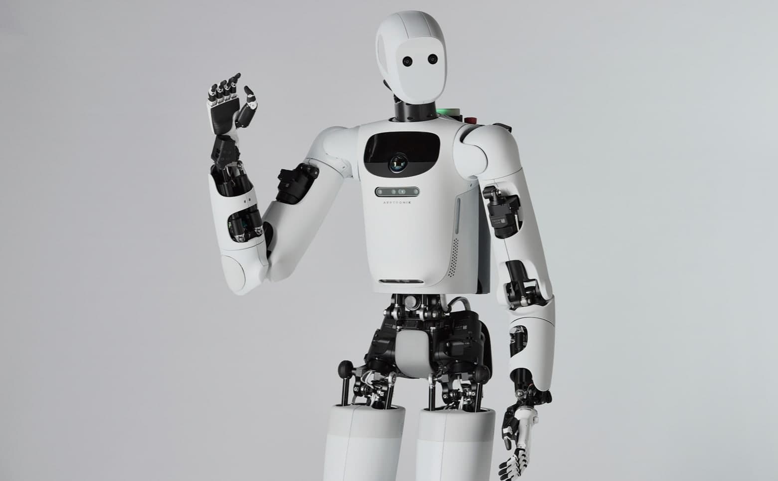 Apptronik's white Apollo humanoid robot, shown from the thighs up against a grey backdrop, raising its right hand.