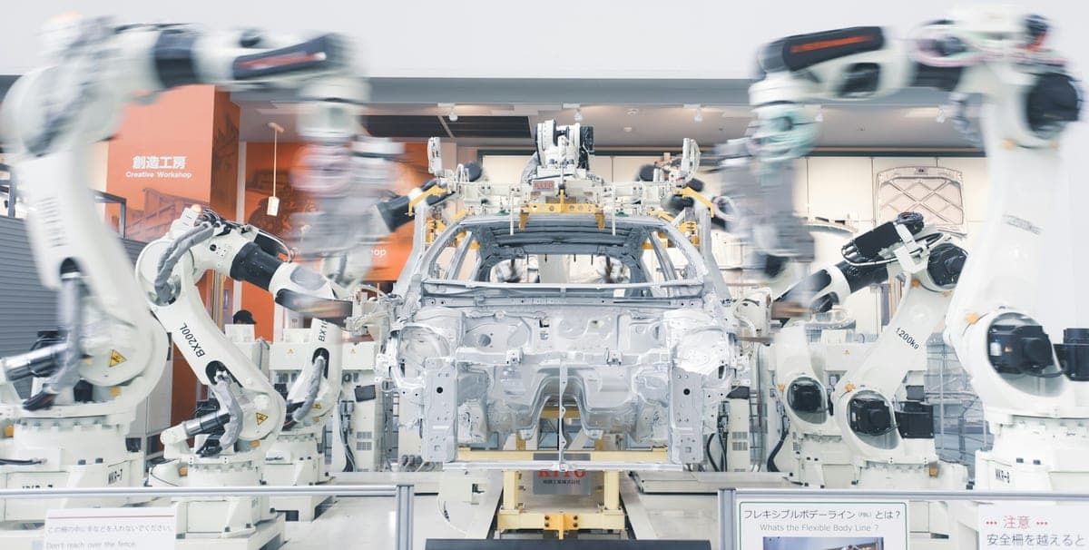 Industrial robot arms working on a bare car body on an automotive assembly line.