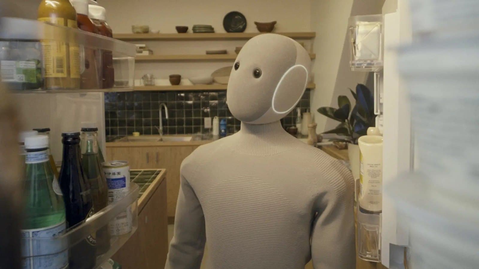 The NEO humanoid robot standing in a home kitchen, seen from inside an open refrigerator.