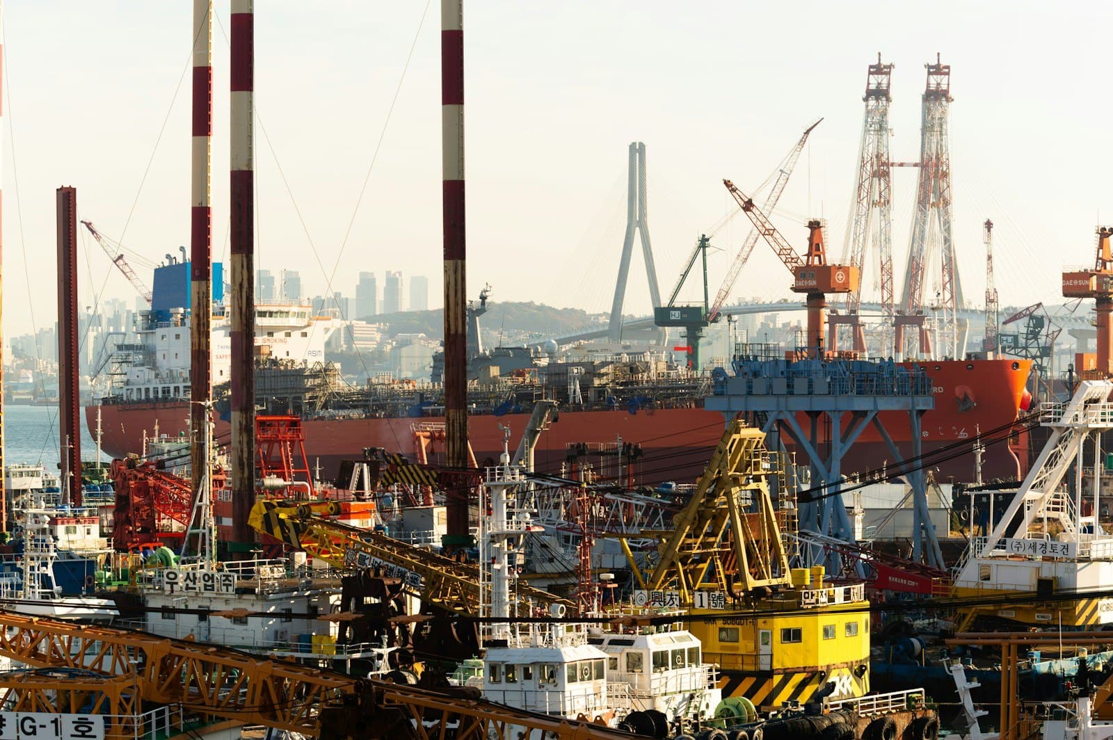 A busy shipyard with ships under construction, cranes and work boats along the waterfront.