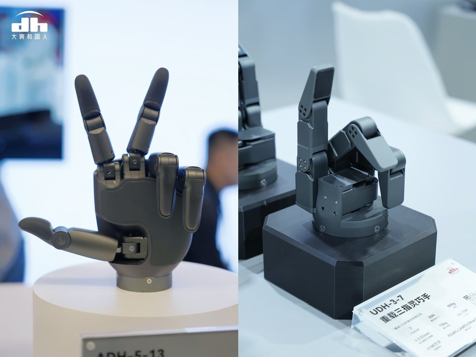 Two dark grey robot hands on display stands: the five-finger ADH-5-13 on the left and the three-finger UDH-3-7 on the right.
