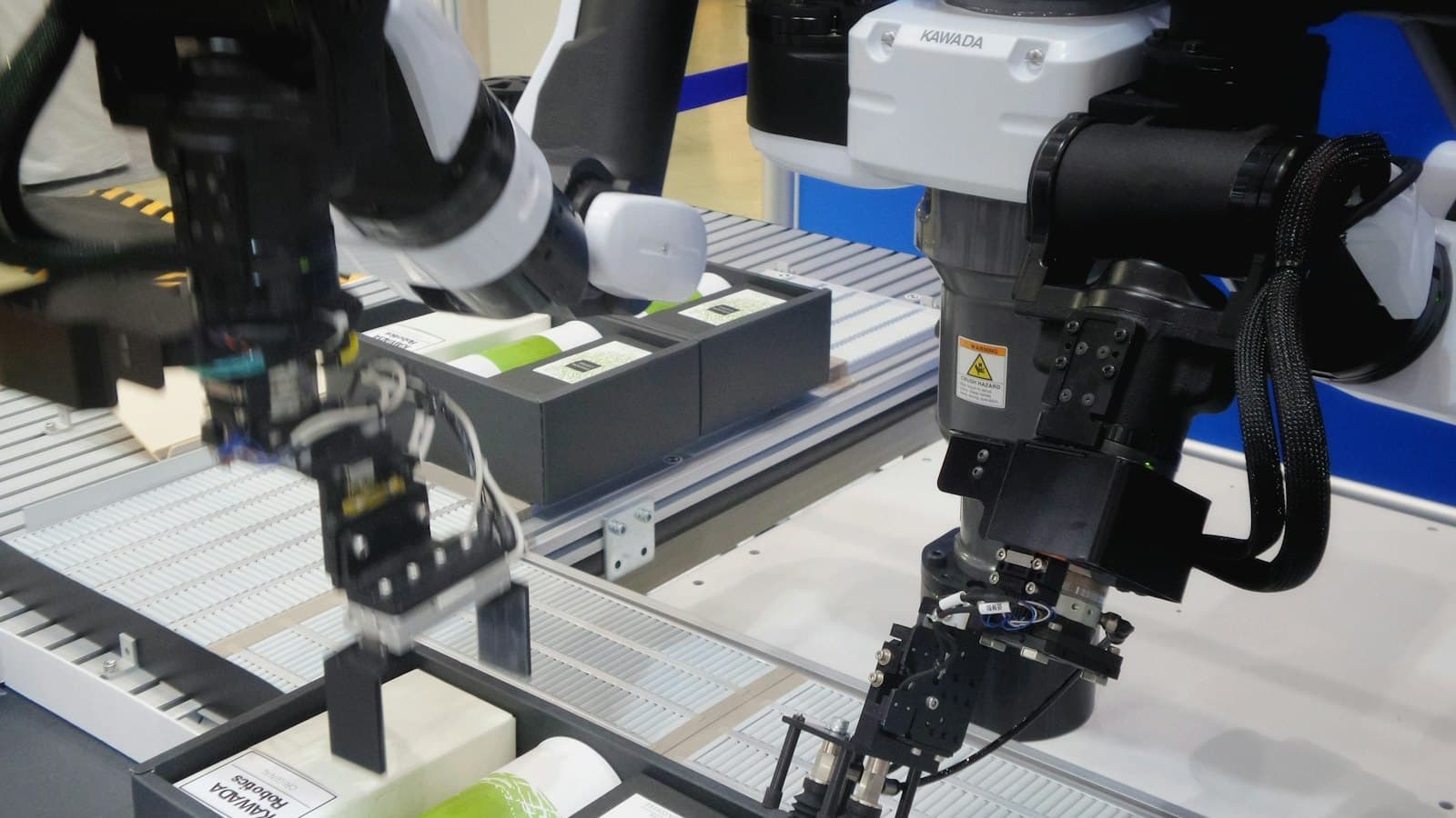 A two-armed robot reaching into bins of small boxes on a conveyor line.