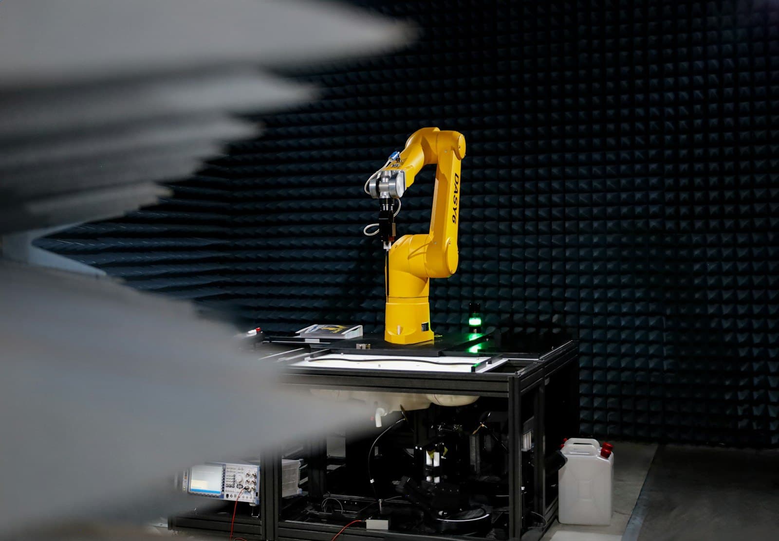 A yellow robot arm mounted on a test bench inside a dark, foam-lined test chamber.