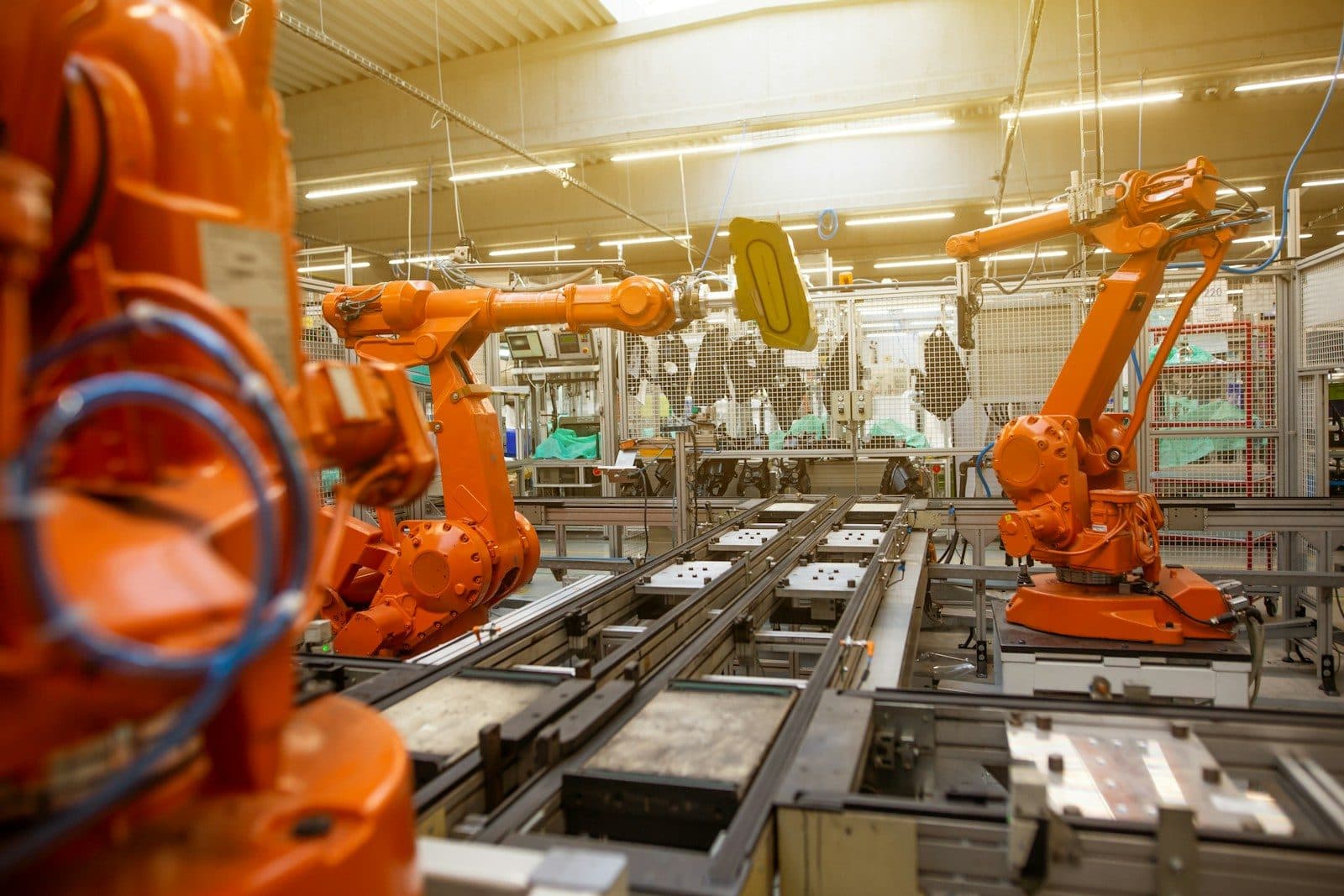 Orange industrial robot arms working on both sides of a parts conveyor in a factory.