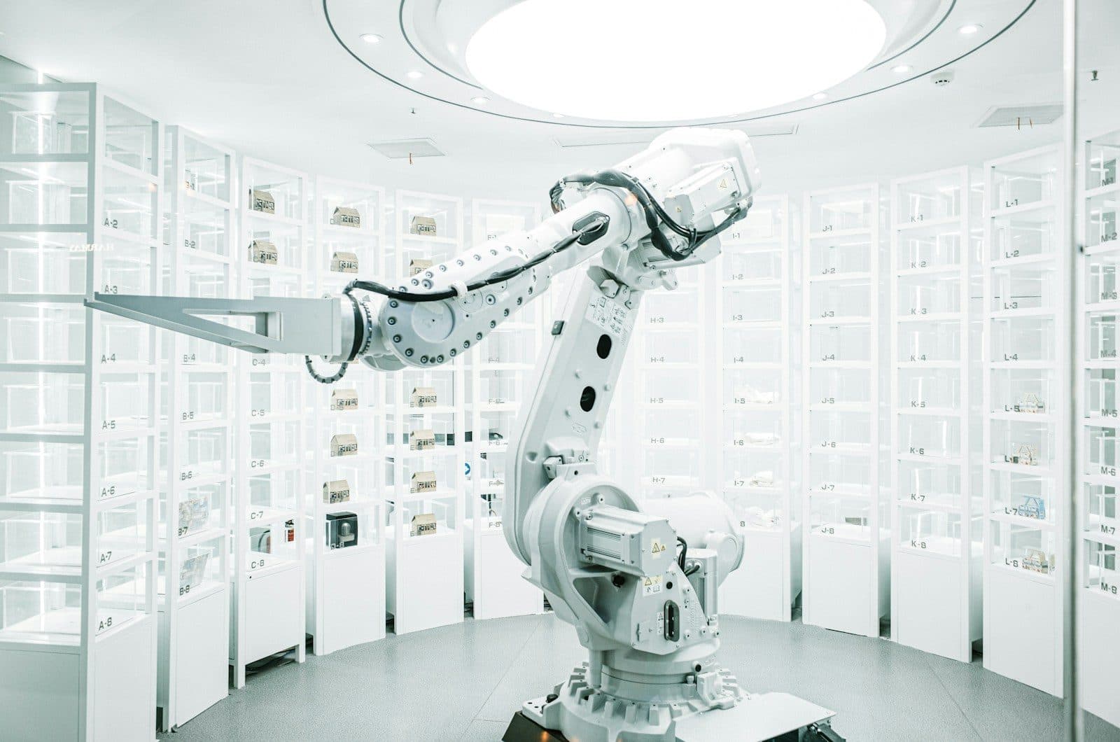 A white industrial robot arm in a bright circular showroom lined with numbered glass display cabinets.