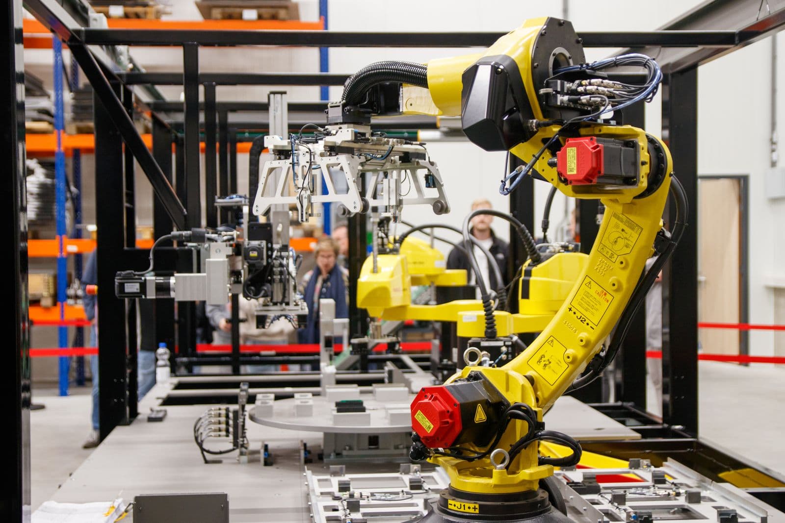 A yellow industrial robotic arm mid-task on a manufacturing floor.