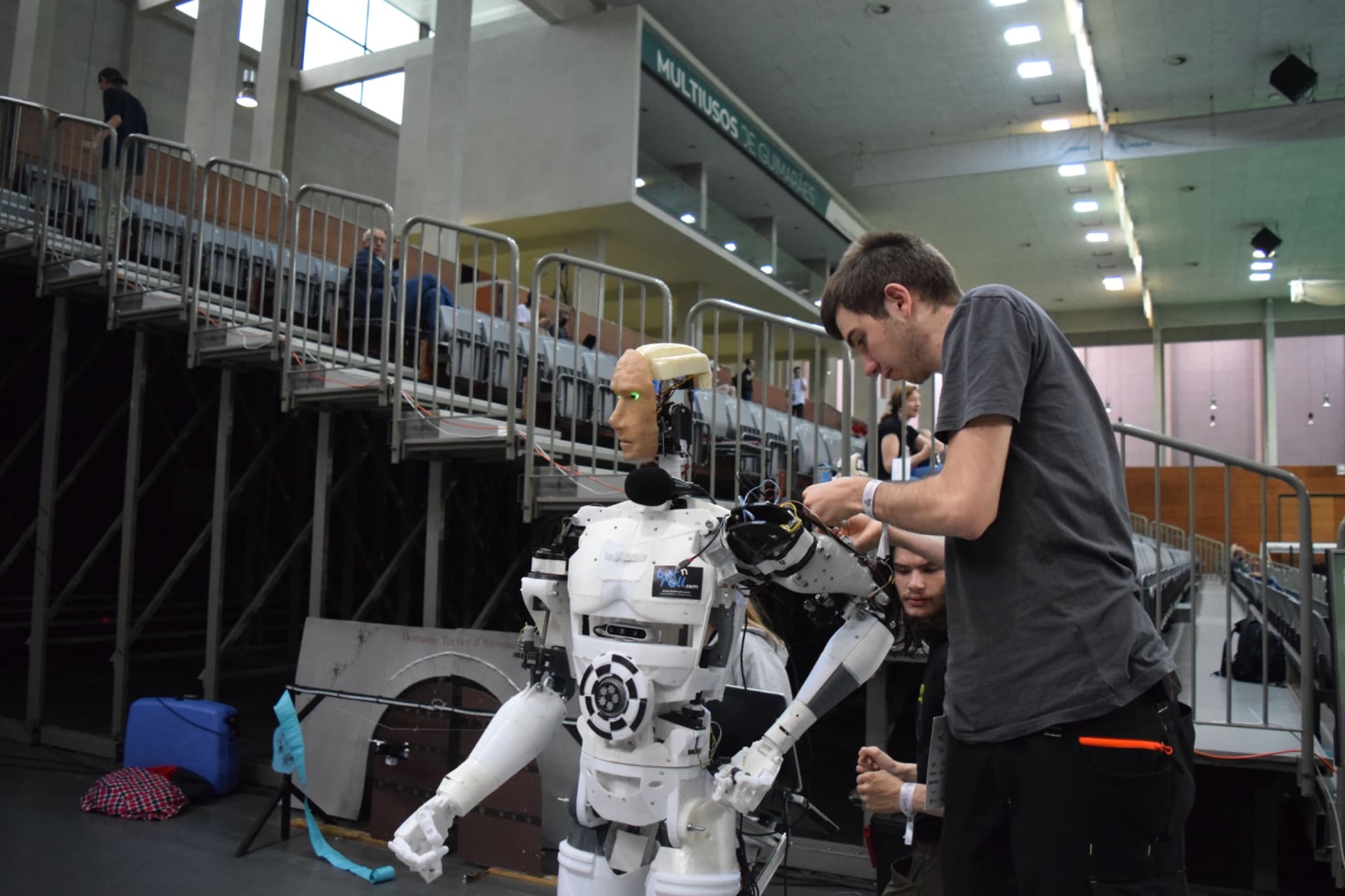 An engineer adjusting the arm of a life-sized humanoid robot in a hall.